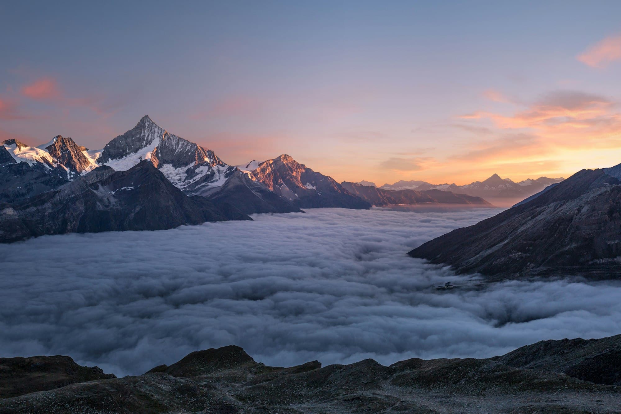 Mountain peaks rising over a sea of clouds at sunset